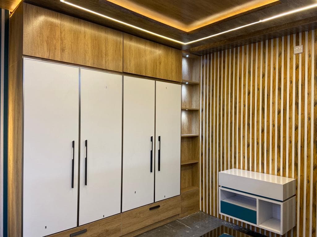 Floor-to-ceiling white RAVYA wardrobe with wood-grain accents and lit open shelving.