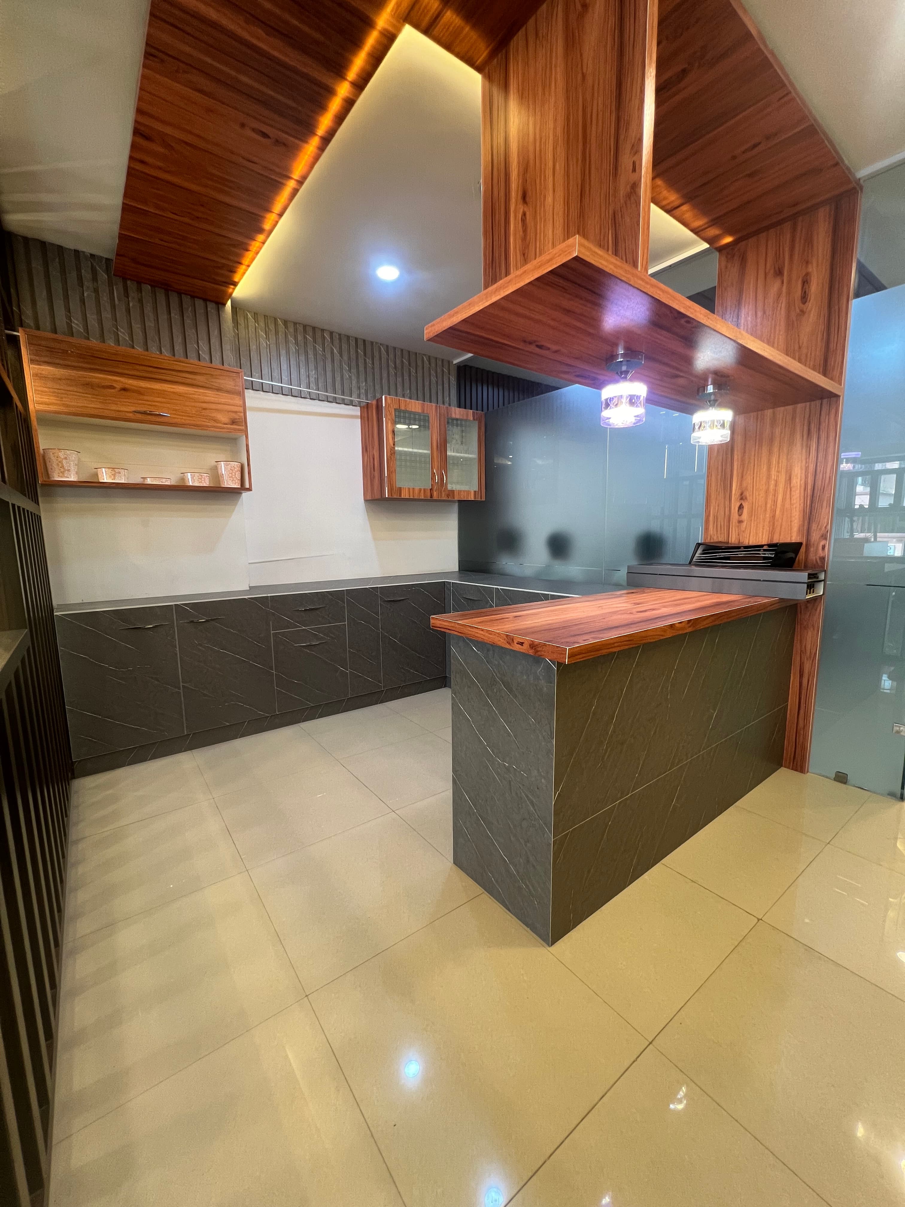 A RAVYA modular kitchen with wood canopy detailing and stone-look cabinetry.