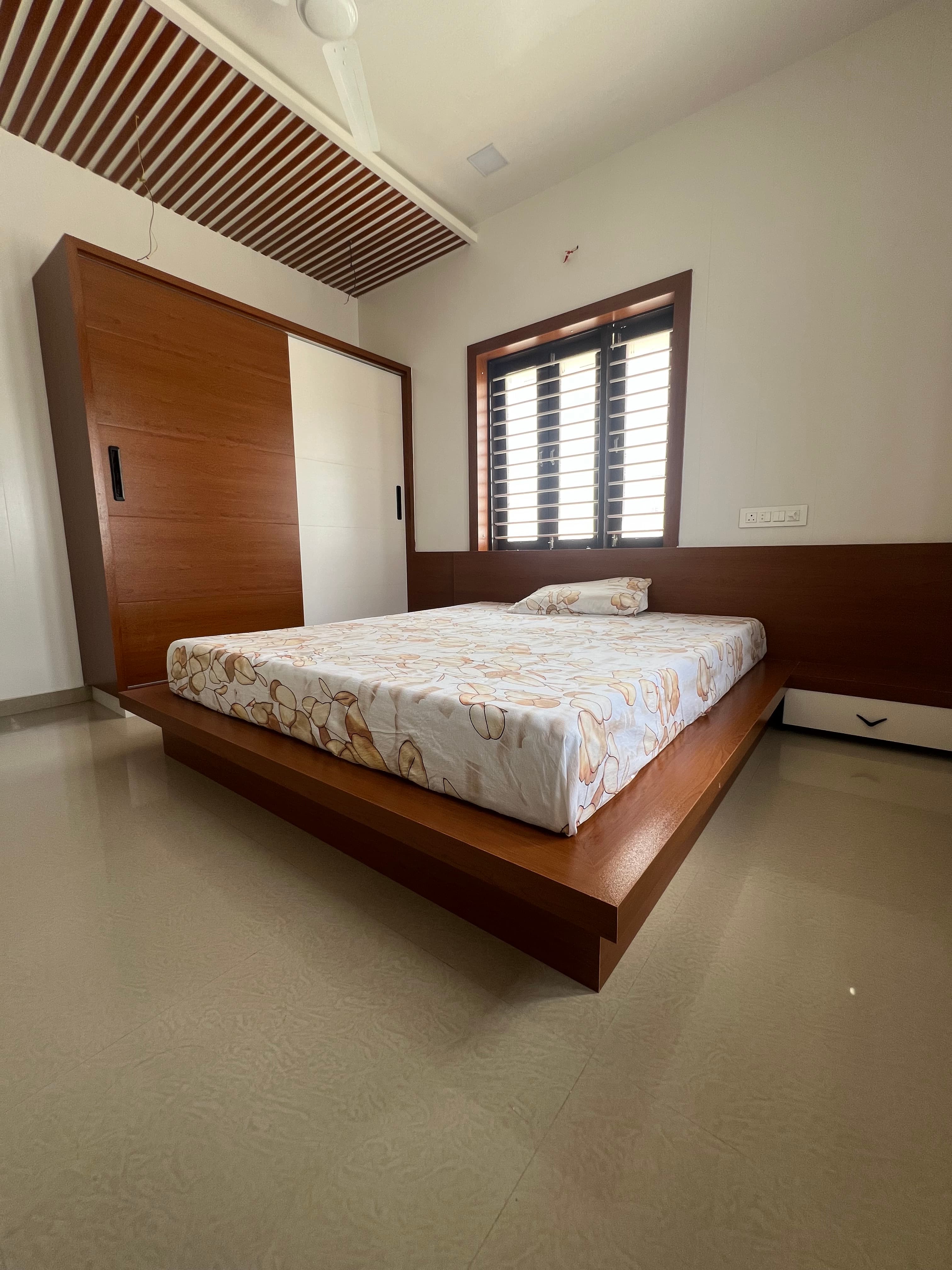 Warm bedroom with platform bed, sliding wardrobe and slatted ceiling detail.