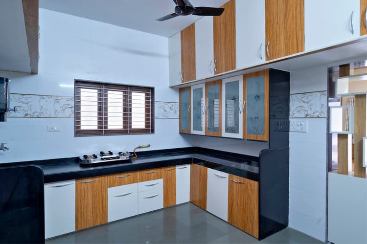 White and wood-grain L-shaped modular kitchen with black granite.