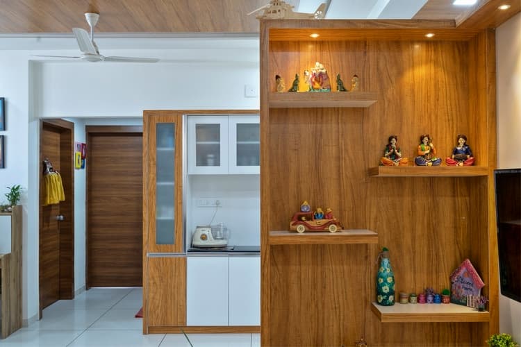 Wood display partition with illuminated shelves beside kitchen cabinetry.